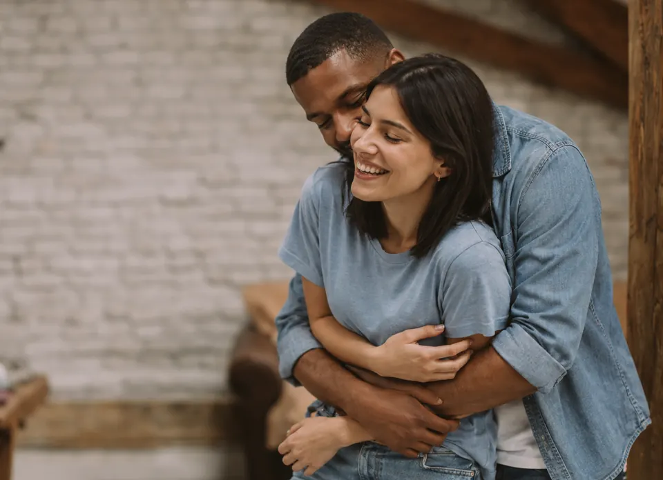 A man in a denim shirt hugging a smiling woman from behind