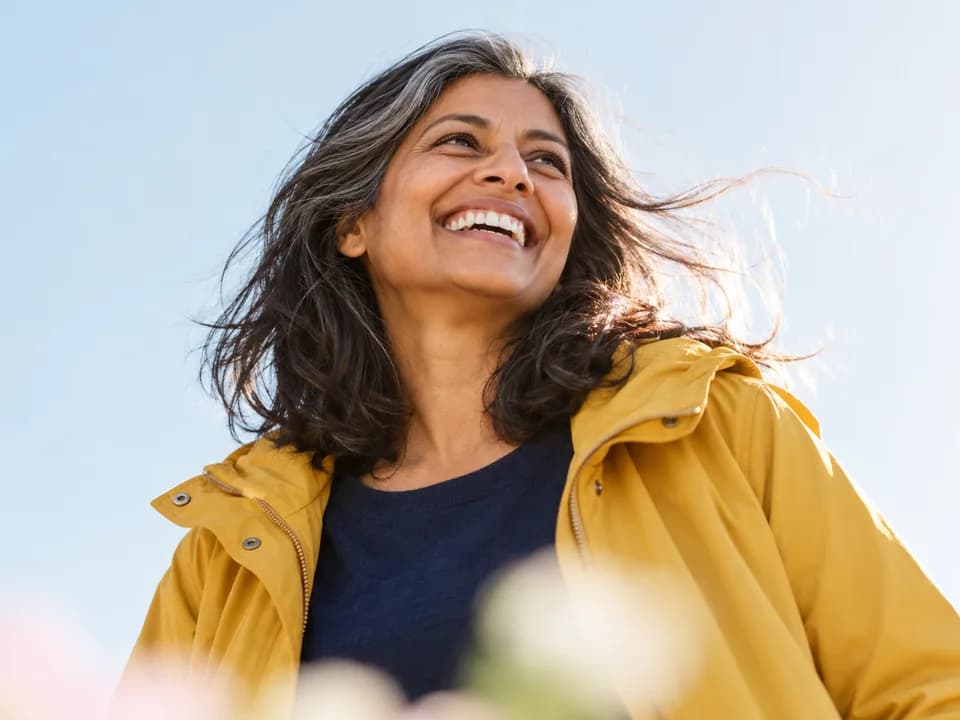 A woman with grey-streaked hair in a yellow raincoat laughing in the wind
